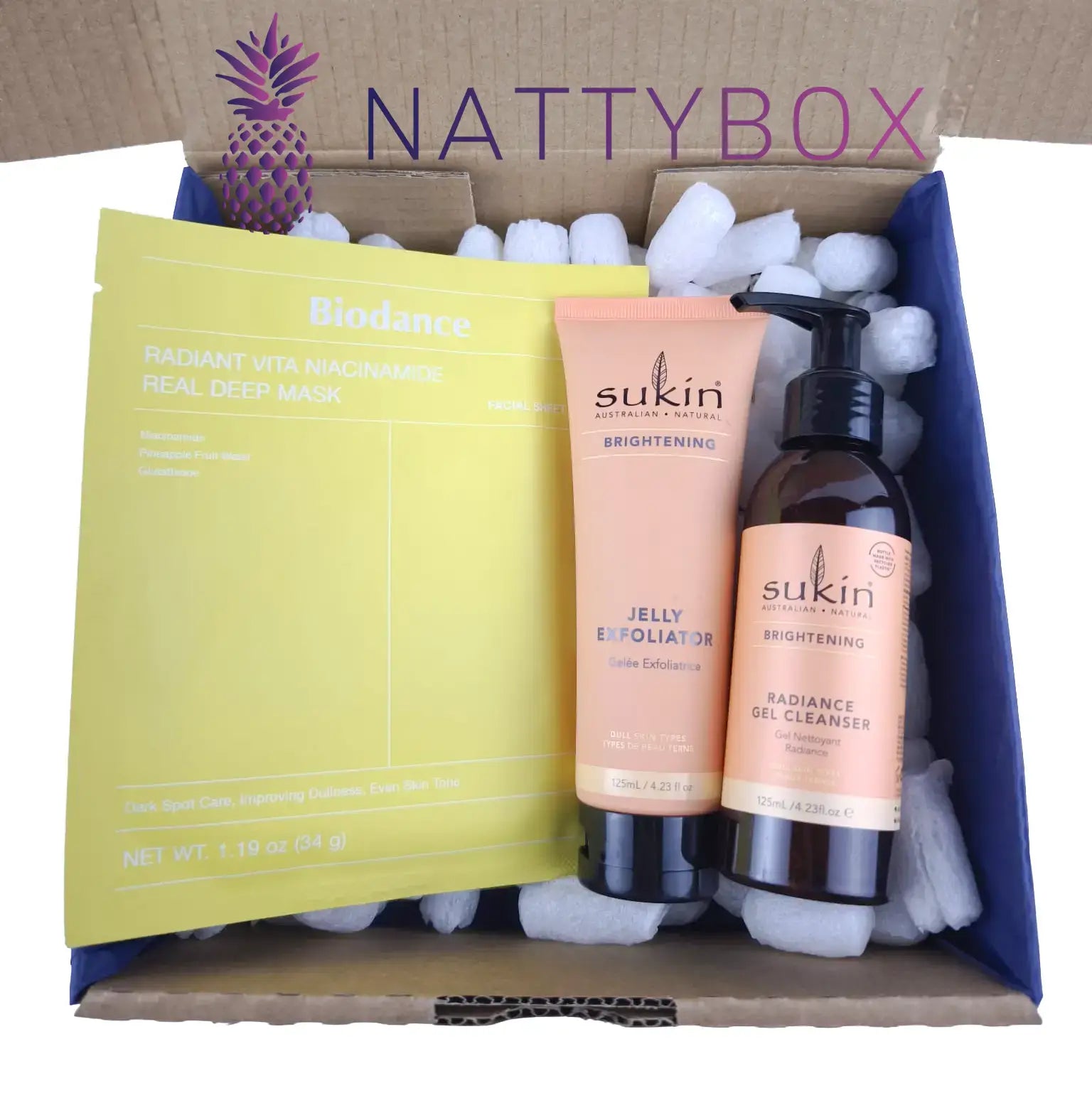 Nattybox with skincare products including a yellow mask, pink exfoliator, and brown cleanser.
